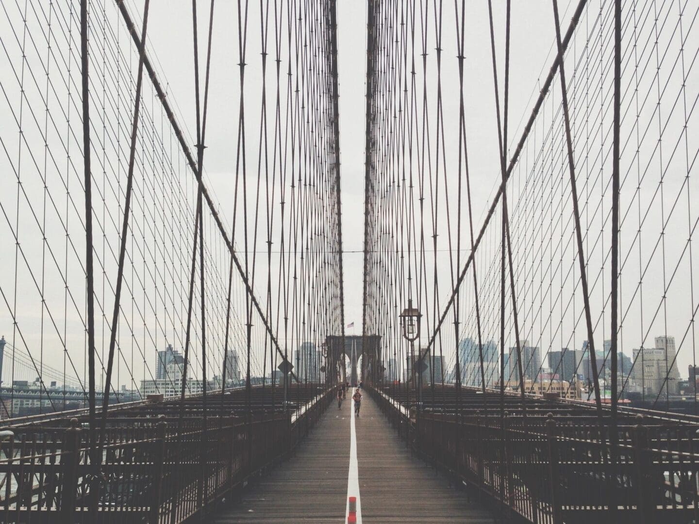 Symmetrical view of a pedestrian pathway on the brooklyn bridge with suspension cables converging in the distance.