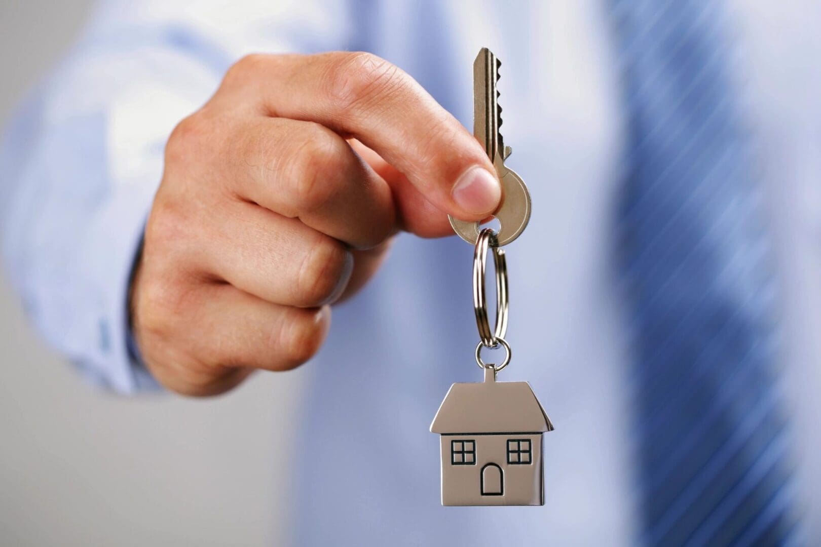 A person in a business suit holding a keychain with a house-shaped key fob.