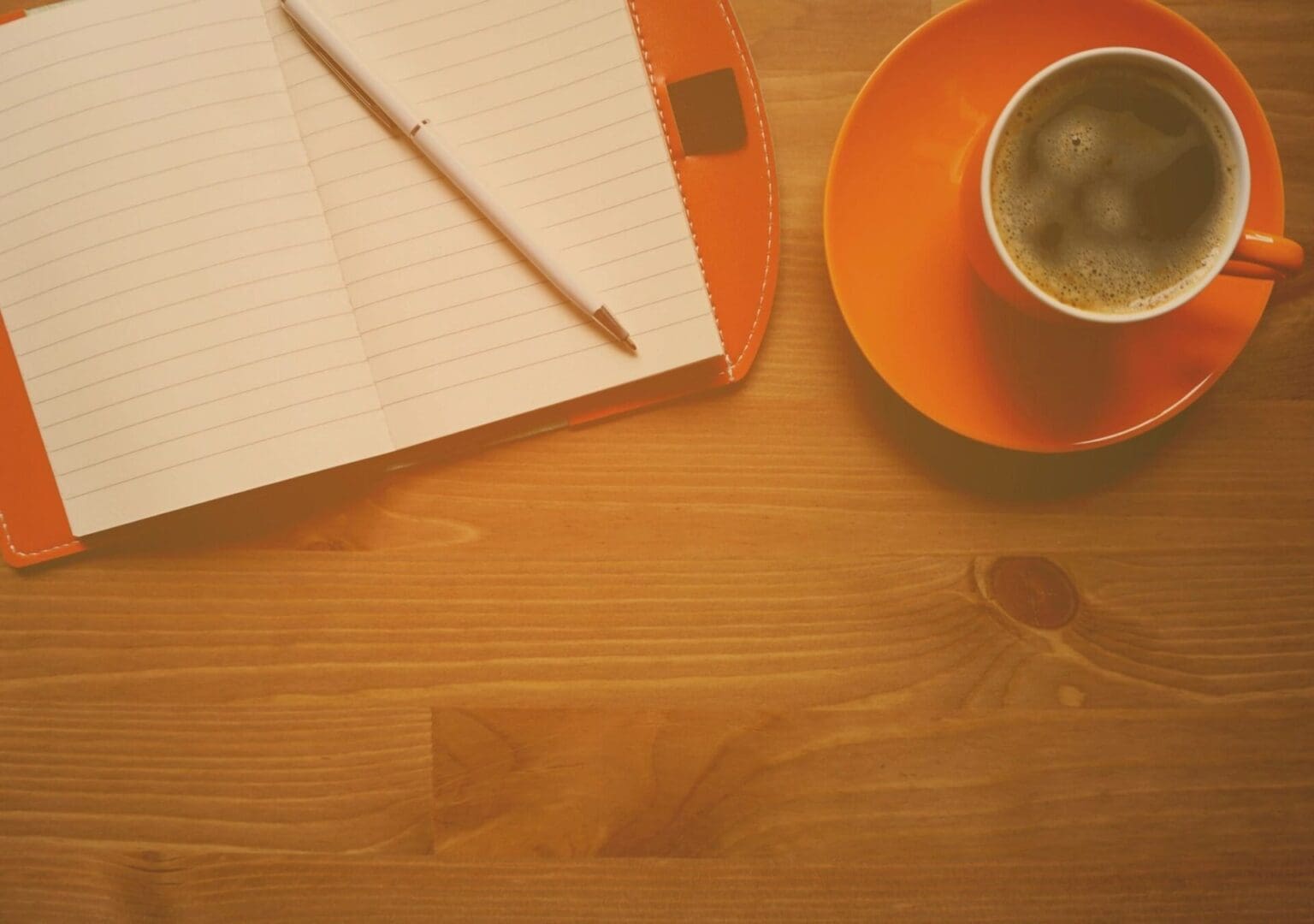 Open notebook with pen and a cup of coffee on a wooden table.
