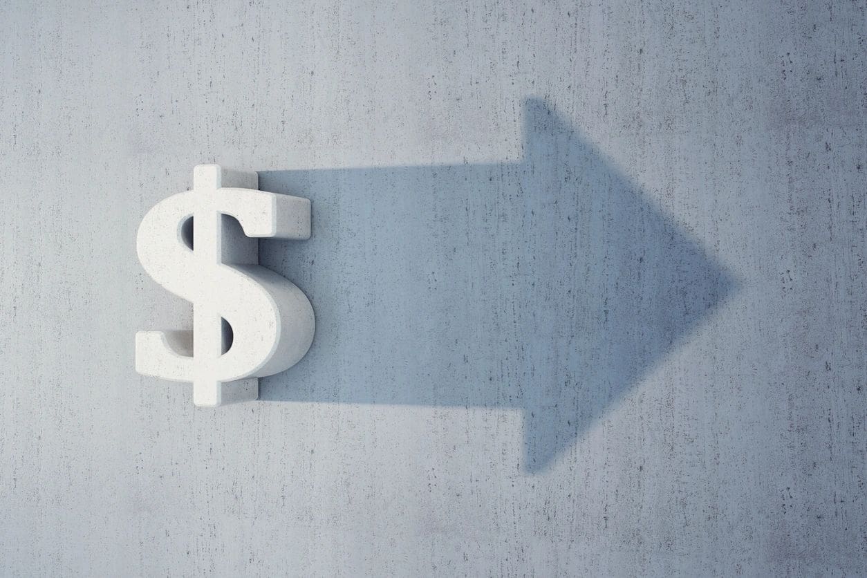 Dollar sign casting a shadow in the shape of an upward arrow on a light gray surface.