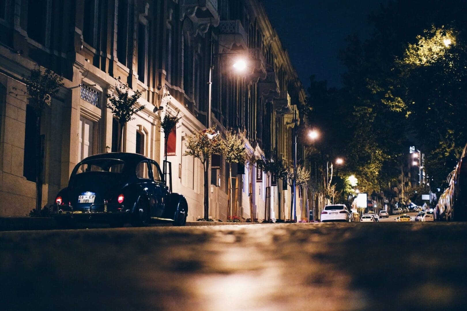 A vintage car parked on a quiet city street at night, illuminated by streetlights.