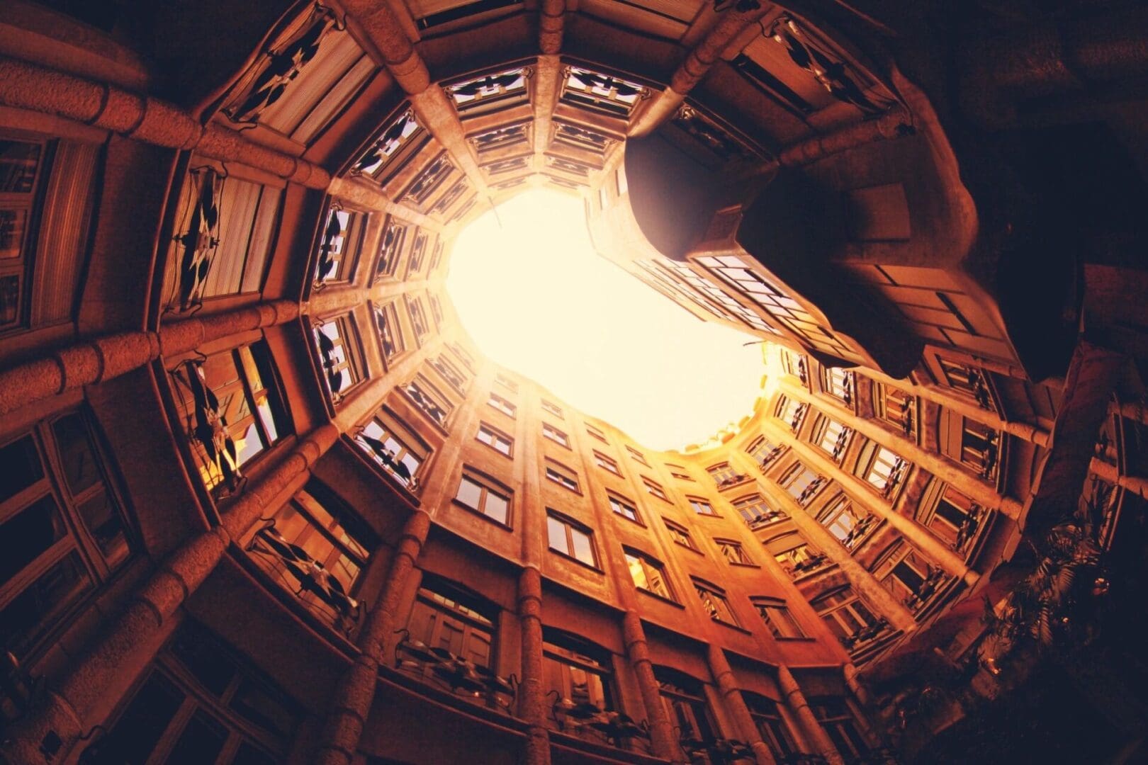 Looking up at a circular courtyard surrounded by ornate buildings with the sun shining directly above.