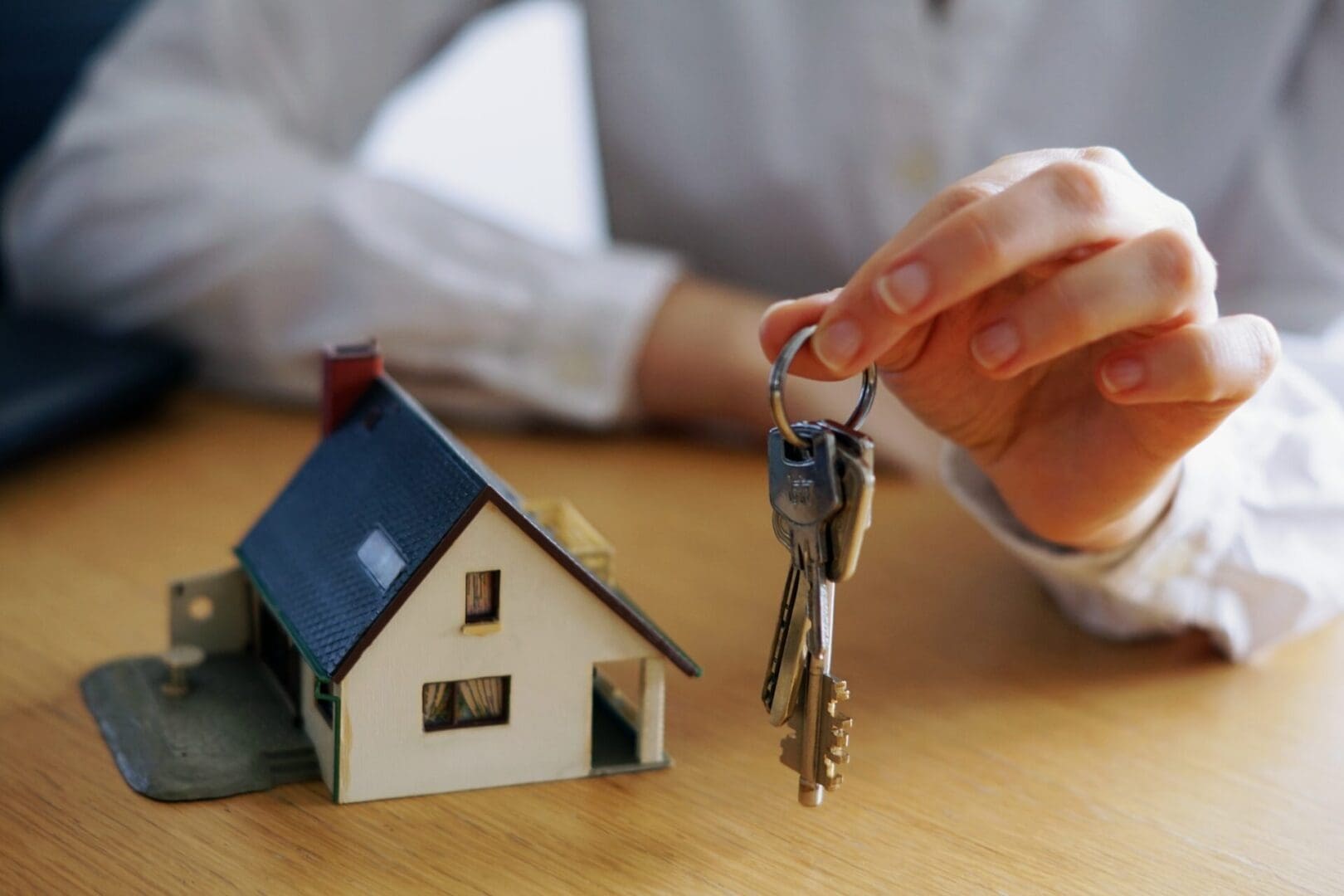 Person holding a set of keys next to a miniature house model, symbolizing Islamic leasing or real estate transaction.