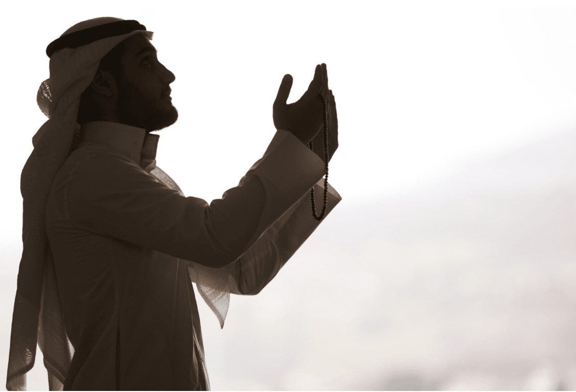Silhouette of a man in traditional Arab attire with hands raised in prayer during Ramadan.