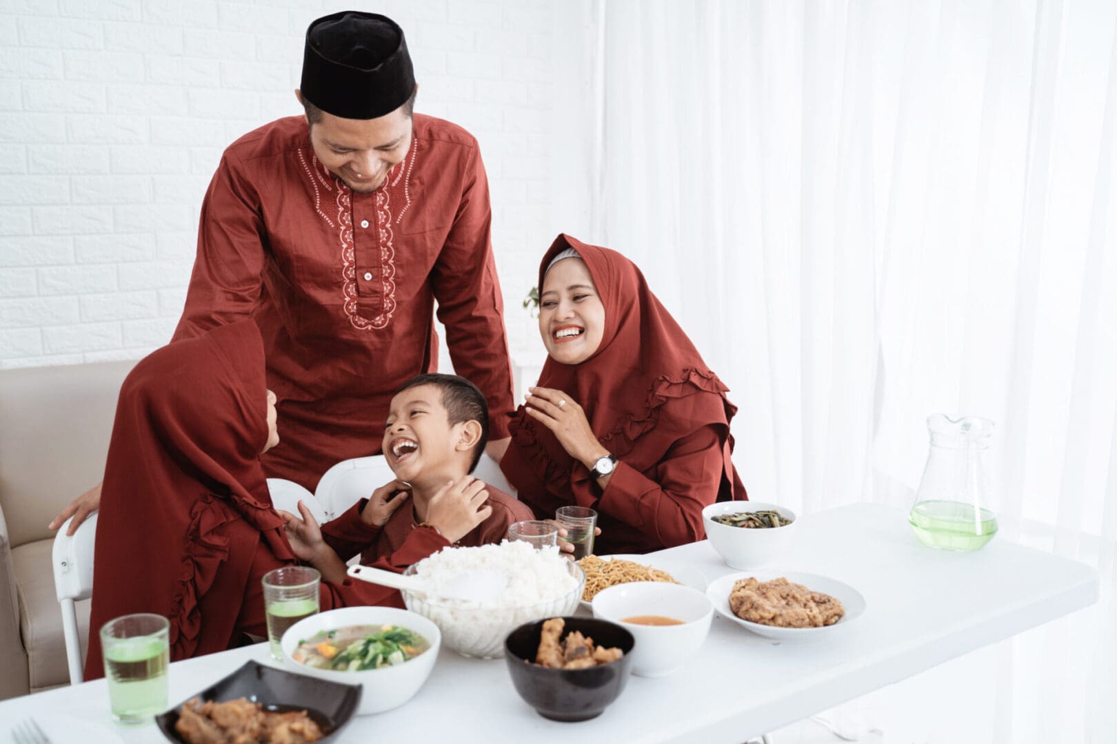 A family dressed in red traditional attire sharing a joyful moment around a dining table with Eid food.