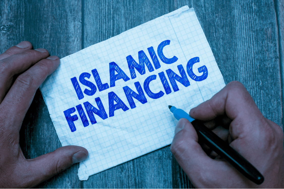 A person writing the words "Islamic Financing" on a piece of graph paper with a blue marker.
