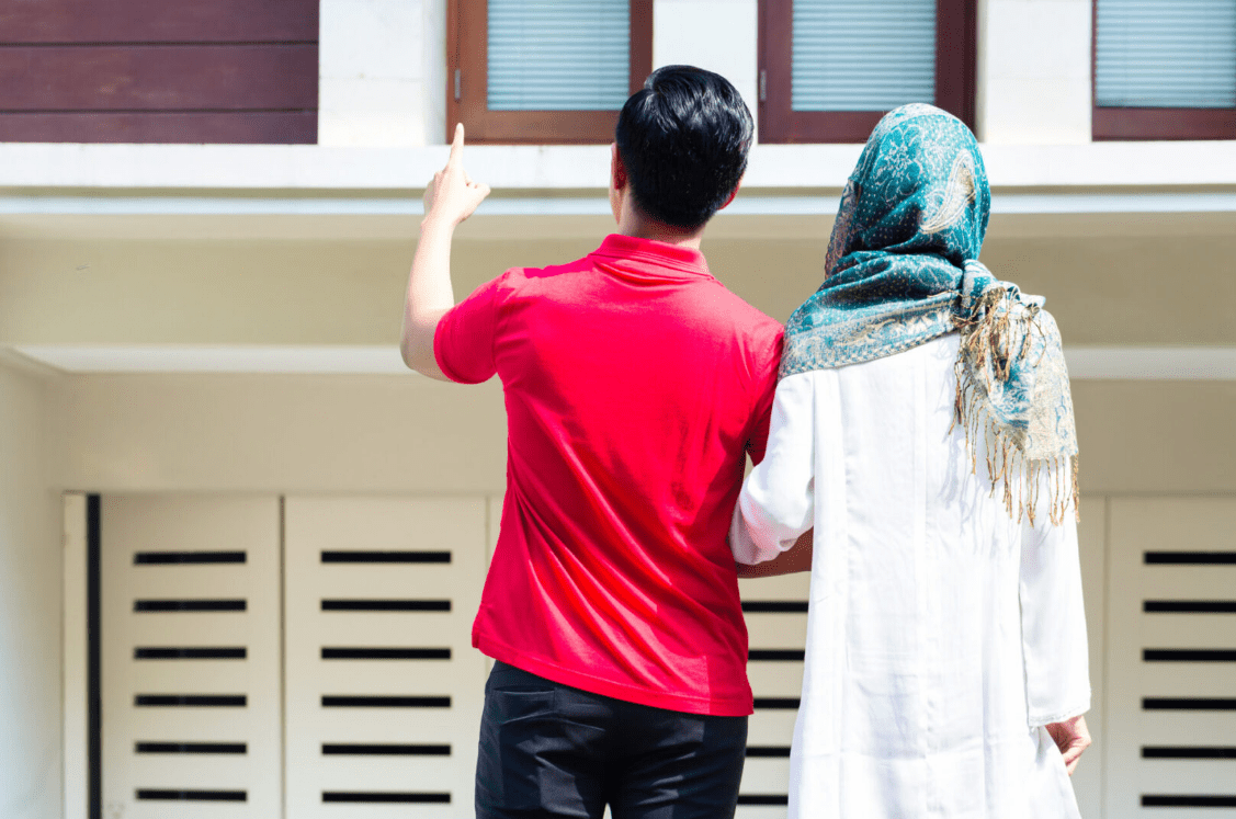 Two people from behind, one pointing upwards, standing in front of their first home.