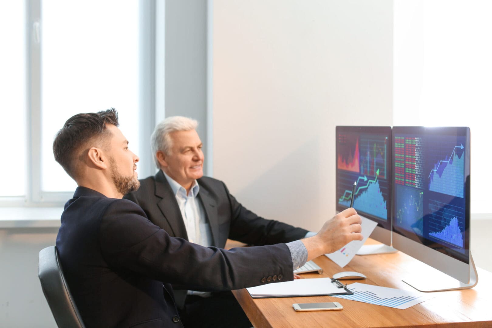 Male brokers working in office. Finance trading concept Two businessmen analyzing residential programs' US financial data on computer screens.