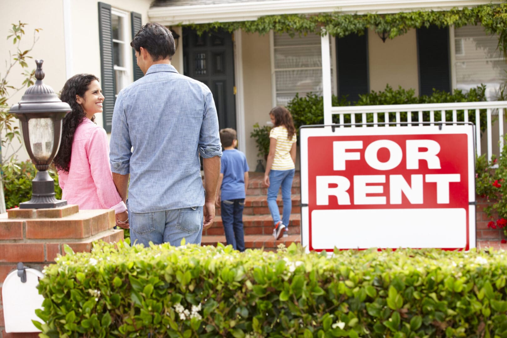Hispanic family outside home for rent Family looking at a house with a "for rent" sign in the front yard, interested in residential programs in the US.