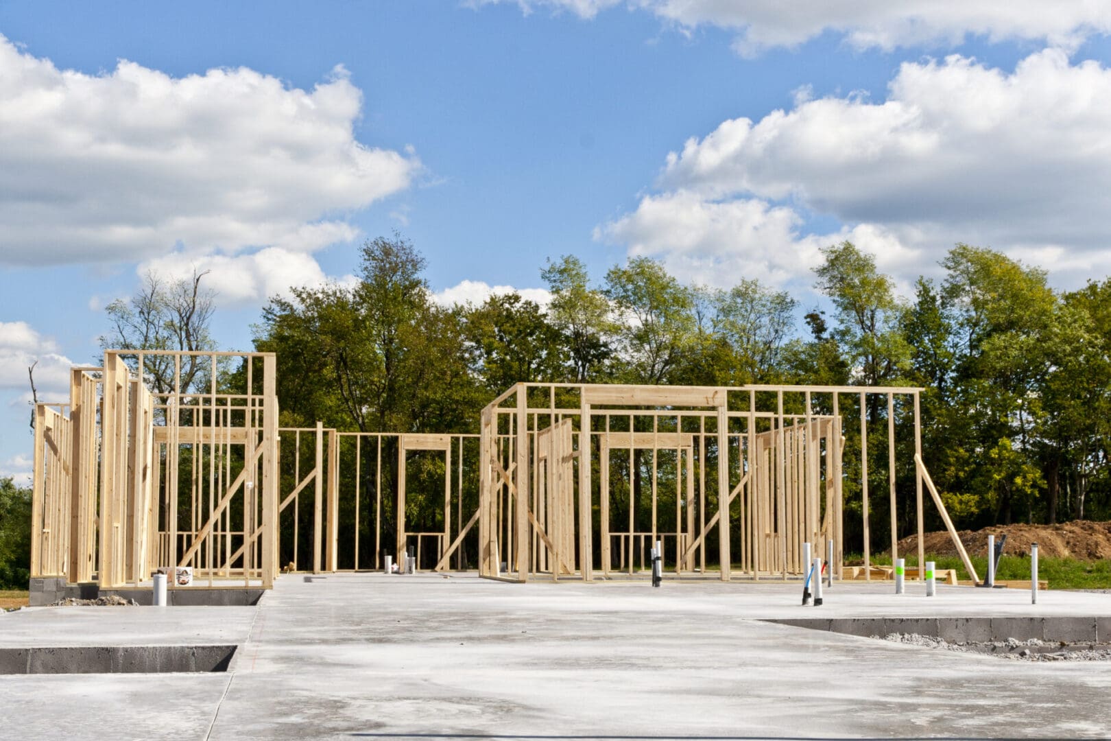 Construction of a new pre-construction home with a wooden frame on a concrete foundation under a partly cloudy sky.