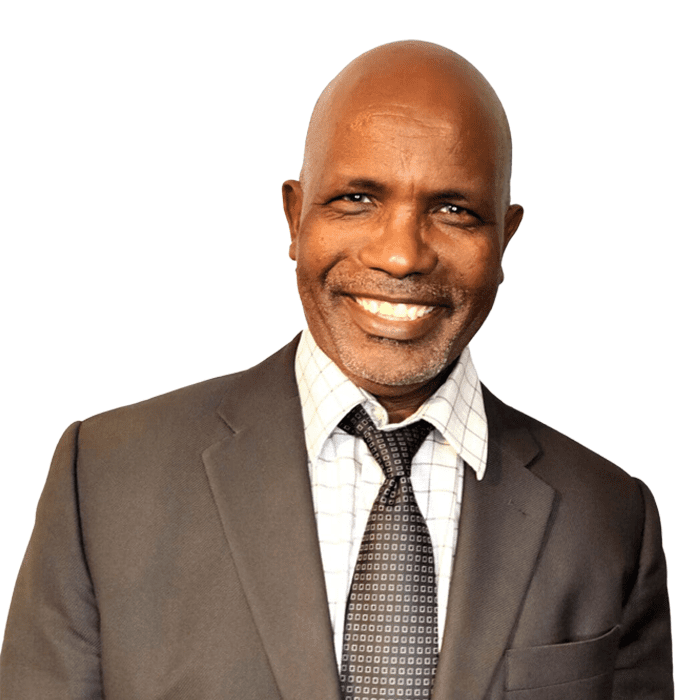 A smiling man in a suit with a preferred checked shirt and patterned tie.