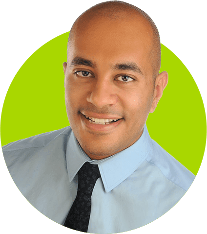 A bald professional man in a light blue shirt and dark tie smiling at the camera with a green background.