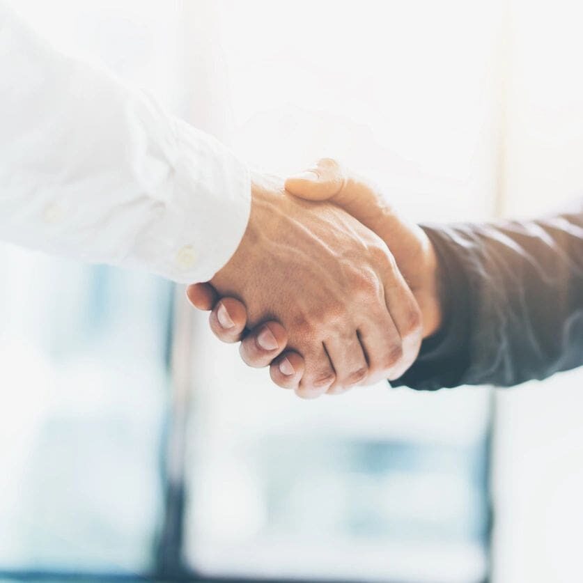 Two individuals shaking hands in a bright residential office environment.