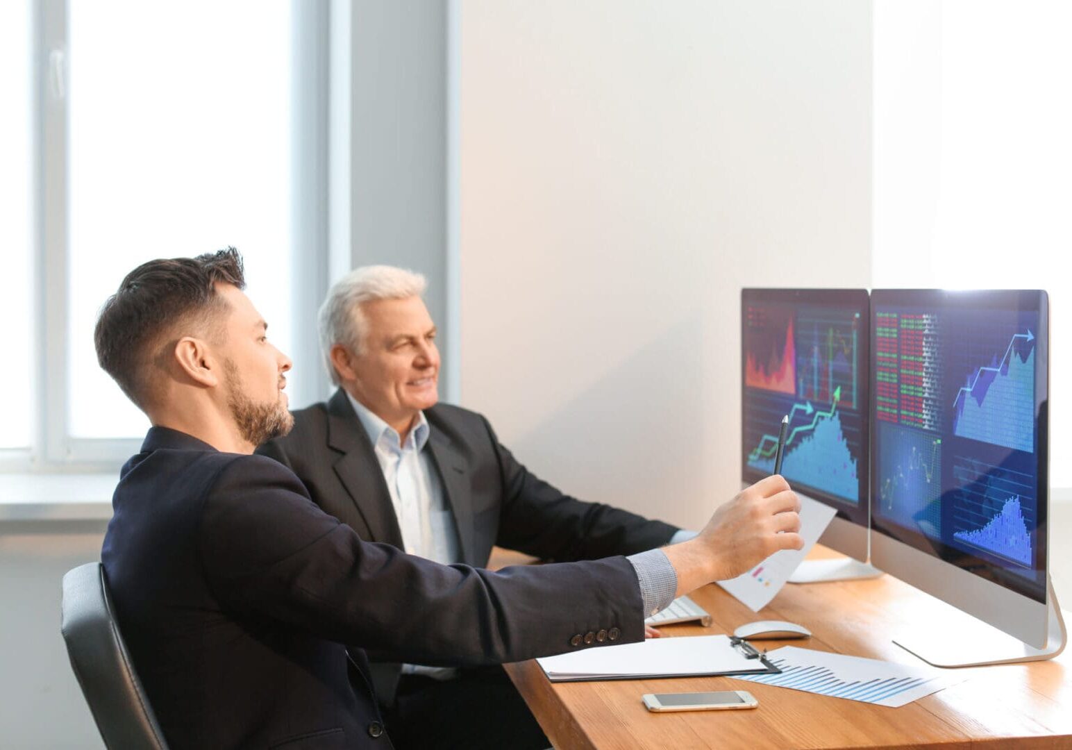 Two businessmen analyzing residential programs' US financial data on computer screens.