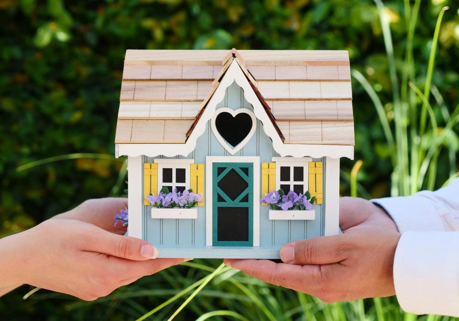 Hands holding a small decorative house.