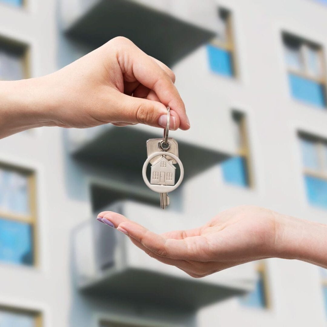 Handover of house keys with apartment building in the background, symbolizing the conversion of ownership.